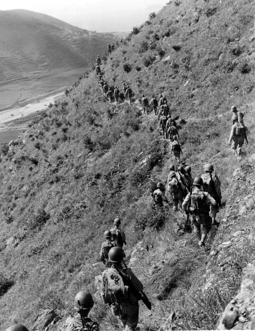 U.S. Marines move out over rugged mountain terrain while closing with hostile North Korean forces